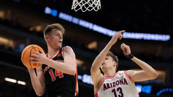 One basketball player in action about to shoot through the hoop while another defends.