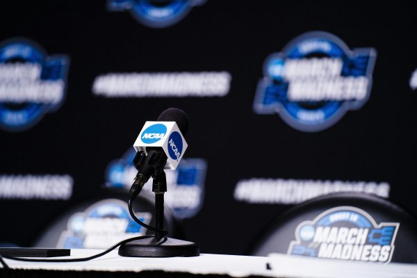 NCAA logo on a microphone against a black background adorned with stickers and signs, symbolizing the thrilling basketball tournament for the NCAA sweet sixteen.