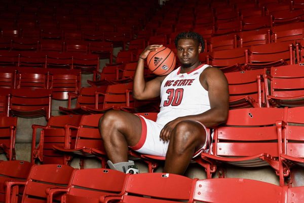 Basketball player sitting in the empty stands holding a basketball on his shoulder. Get ready for the final four.